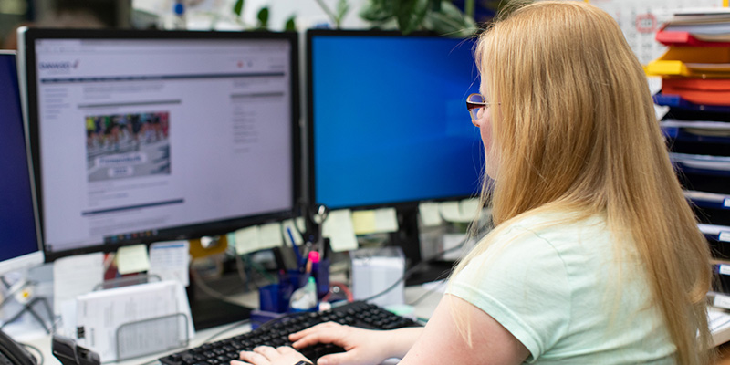 Frau mit blonden langen Haaren und Brille gibt auf der Tastatur Daten ein