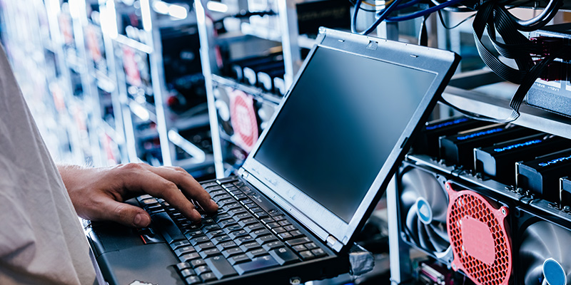 Mann mit einem Laptop in der Hand steht im Serverraum